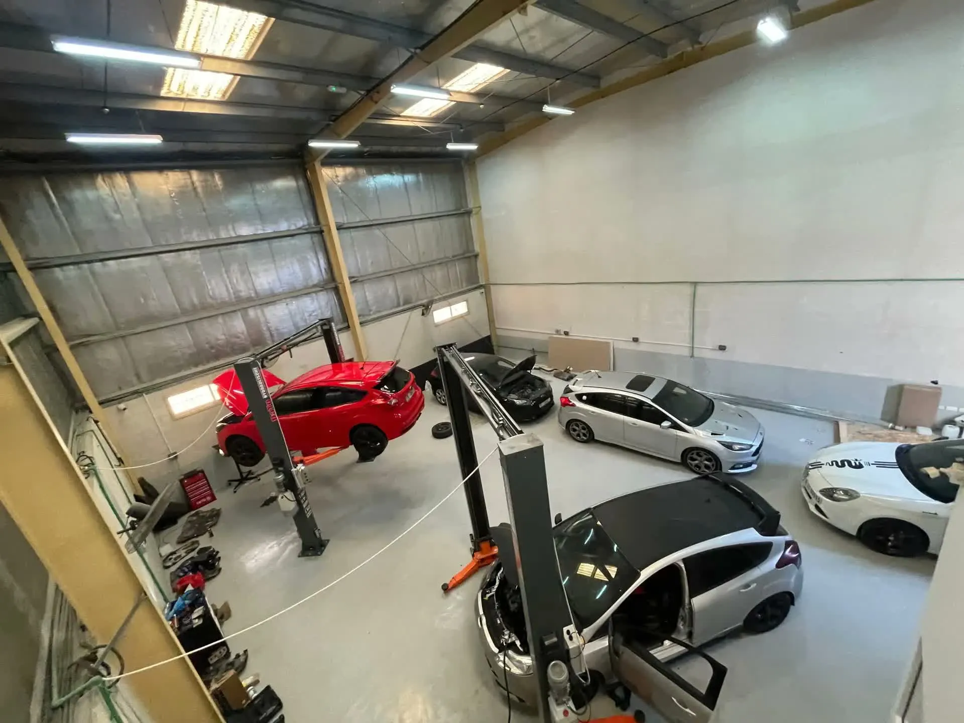 Two Ford Focus hatchbacks raised on two-post lifts inside the RST Werks workshop, with a red Focus ST on the left