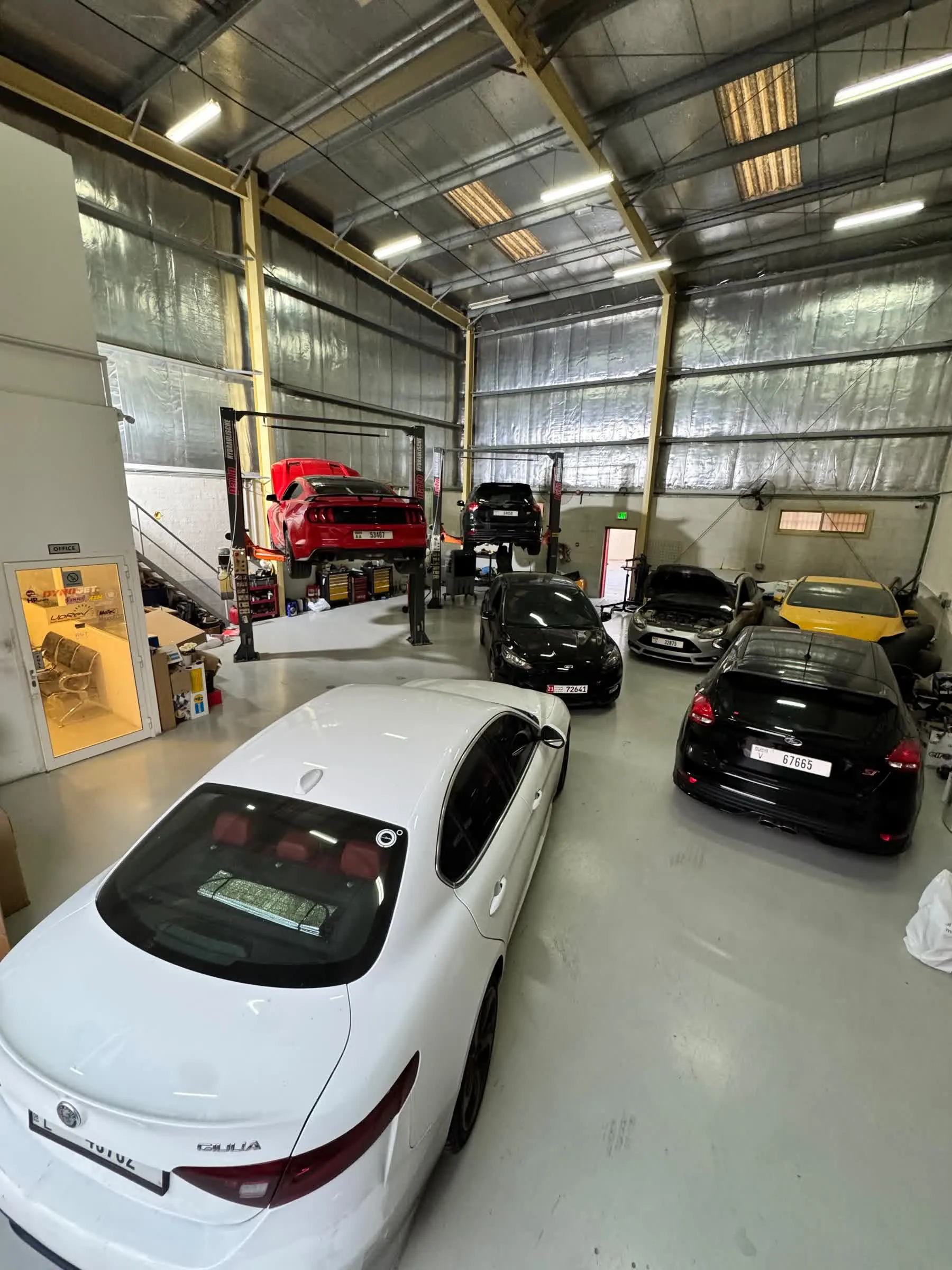 Inside the RST Werks workshop: a white Alfa Romeo Giulia in the foreground with a red Mustang and Ford Focus ST on two-post lifts behind