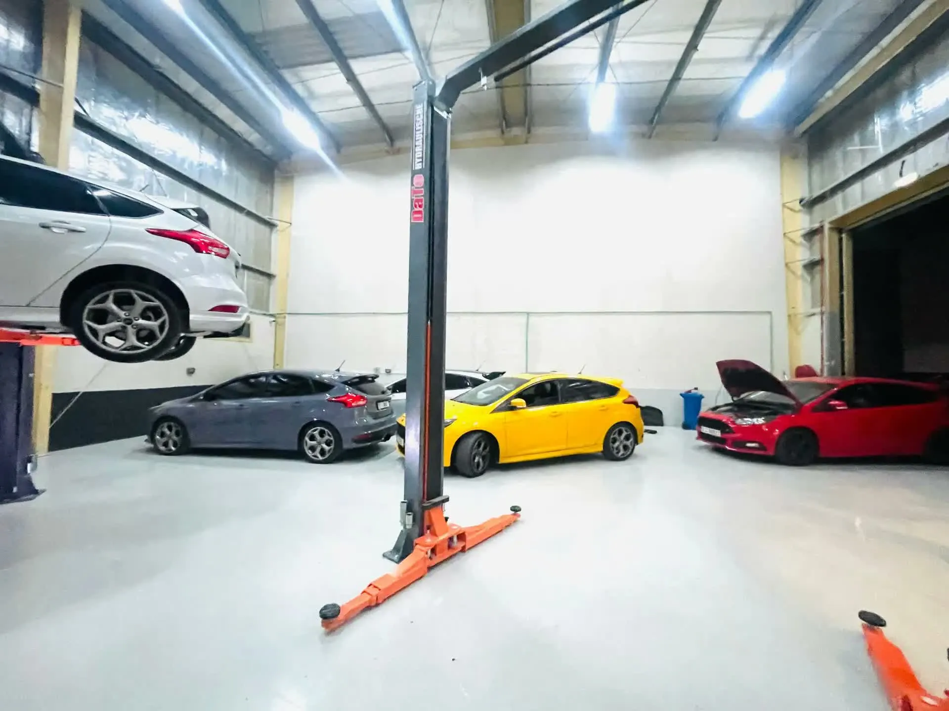 A white Ford Focus ST on a lift beside grey, yellow and red Focus ST hatchbacks in the RST Werks workshop